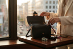 Karryol Mona black leather crossbody bag with gold hardware, adjustable strap, and zip closure. Woman placing lipstick inside.