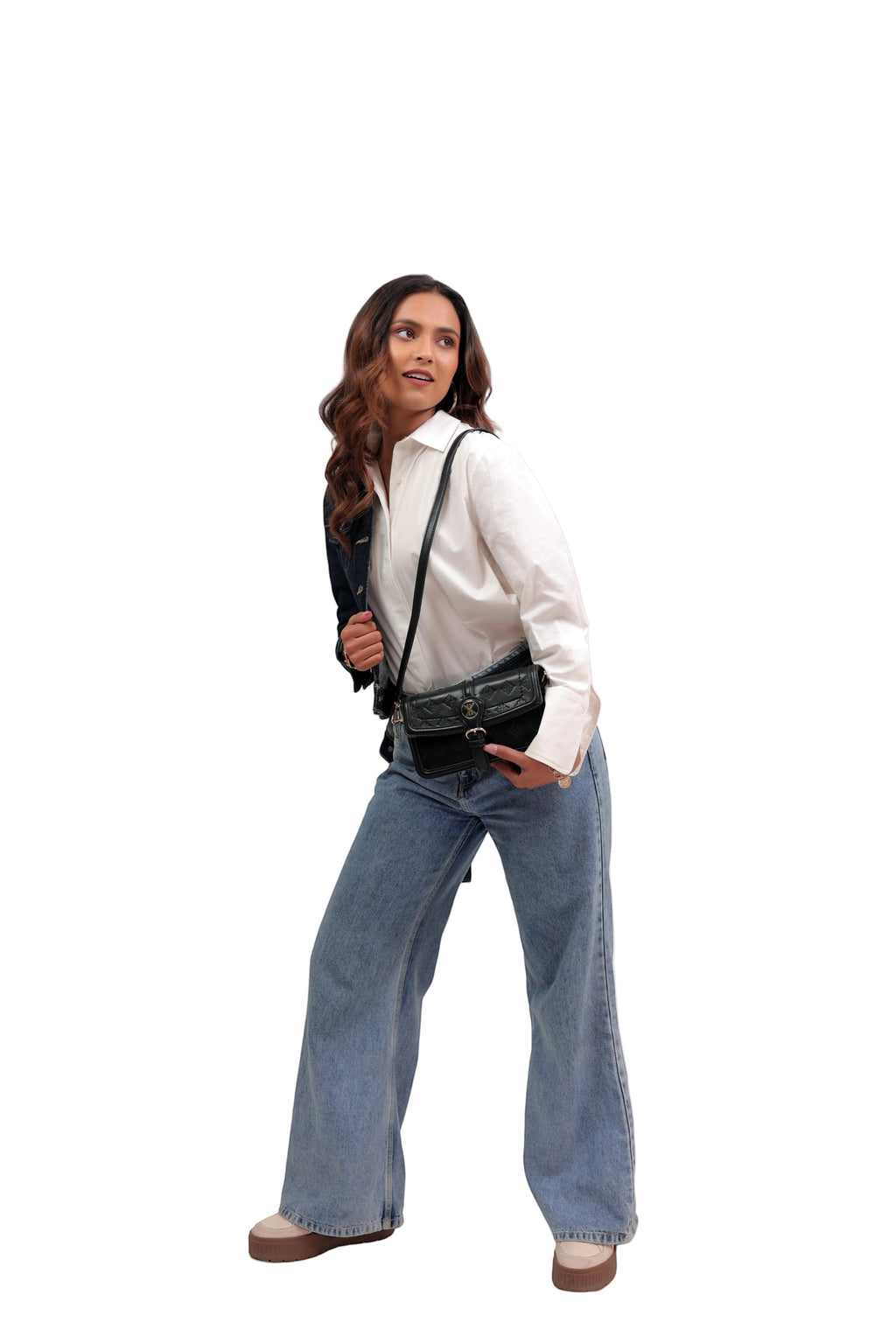KARRYOL black leather Kari crossbody bag with embossed monogram panel and gold-tone hardware, worn by a woman in a white shirt and jeans.