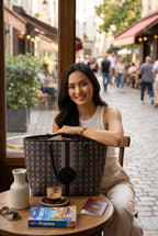 Woman sitting at a cafe table with a black KARRYOL monogram tote bag featuring leather trim and a metal logo plaque.