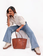 KARRYOL Monica tan leather tote bag with dual top handles and zipper closure, held by a woman in jeans and a white shirt.