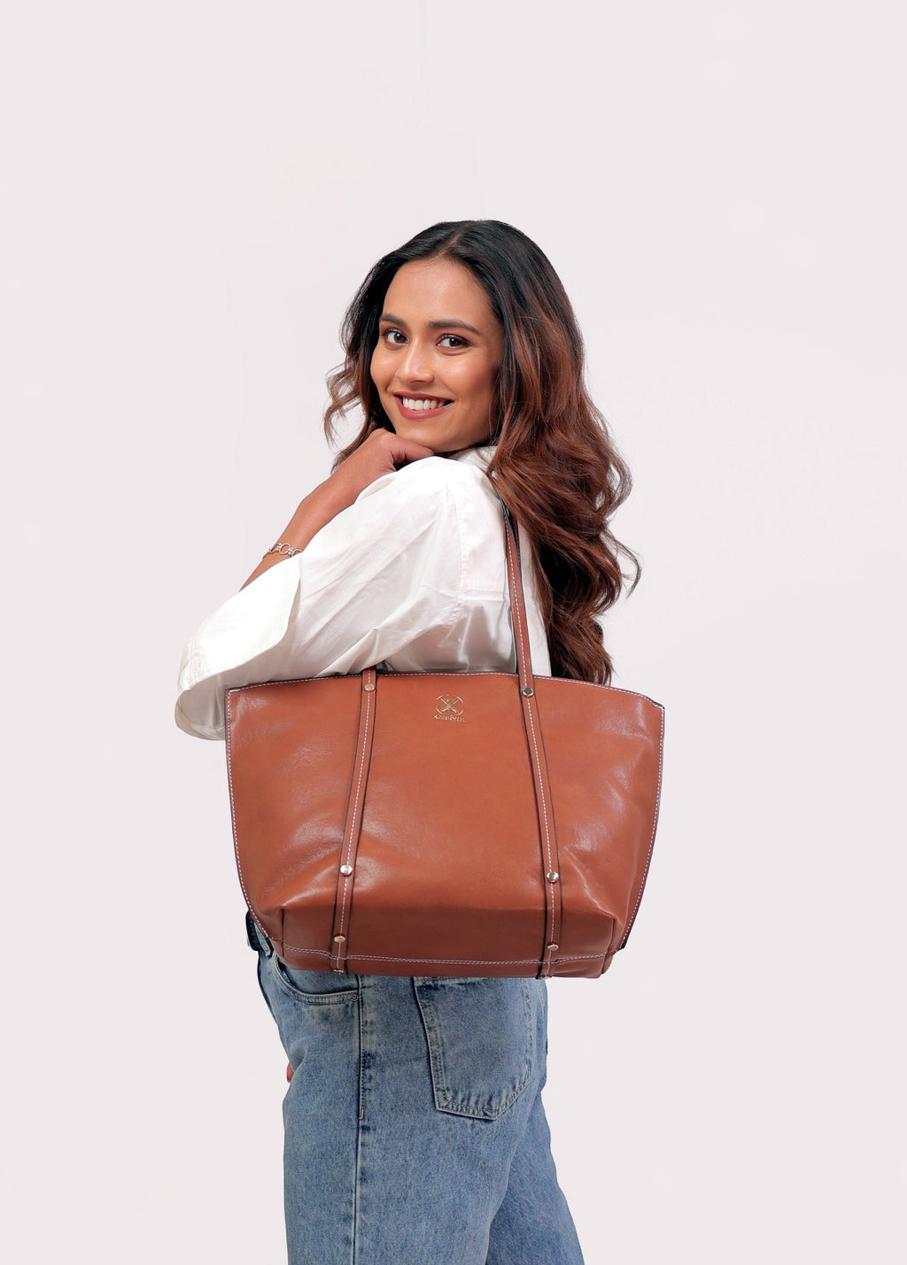 KARRYOL tan leather Monica tote bag with dual top handles and zipper closure, worn by a woman.